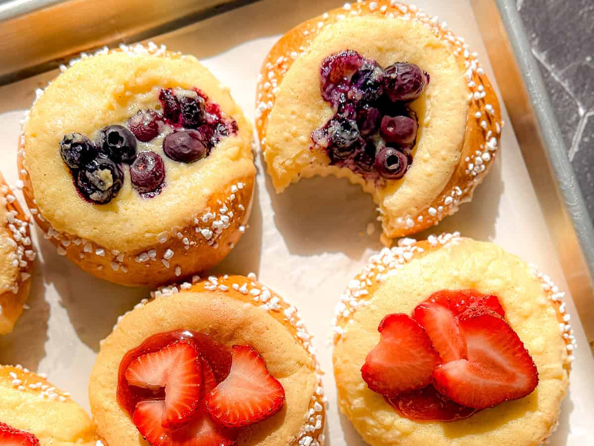 Berry topped brioche danishes on a parchment paper lined sheet pan, one with a bite taken out.