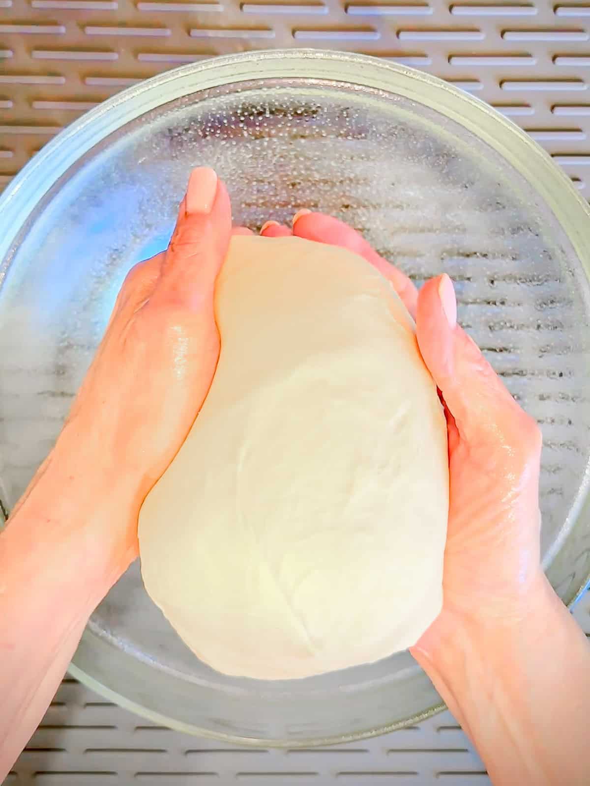 Shaking dough into a ball over a glass bowl.