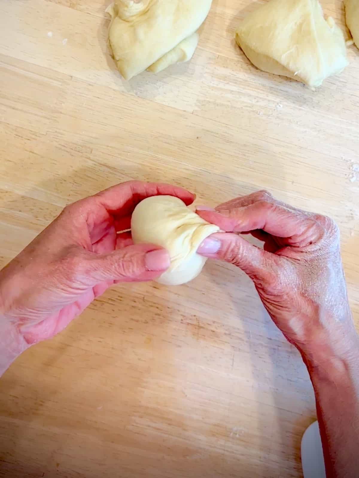 Pinching closed the top of a dough ball.