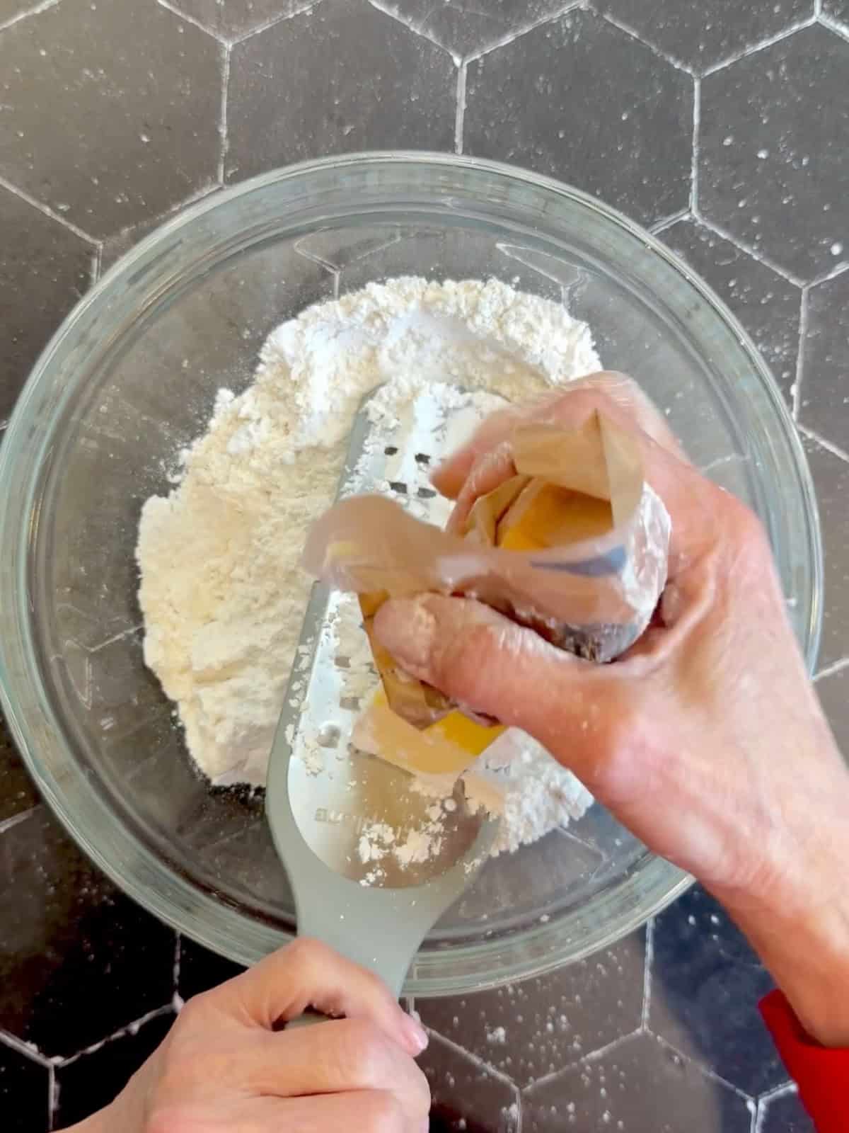 Grating butter into dry ingredients in a glass bowl.