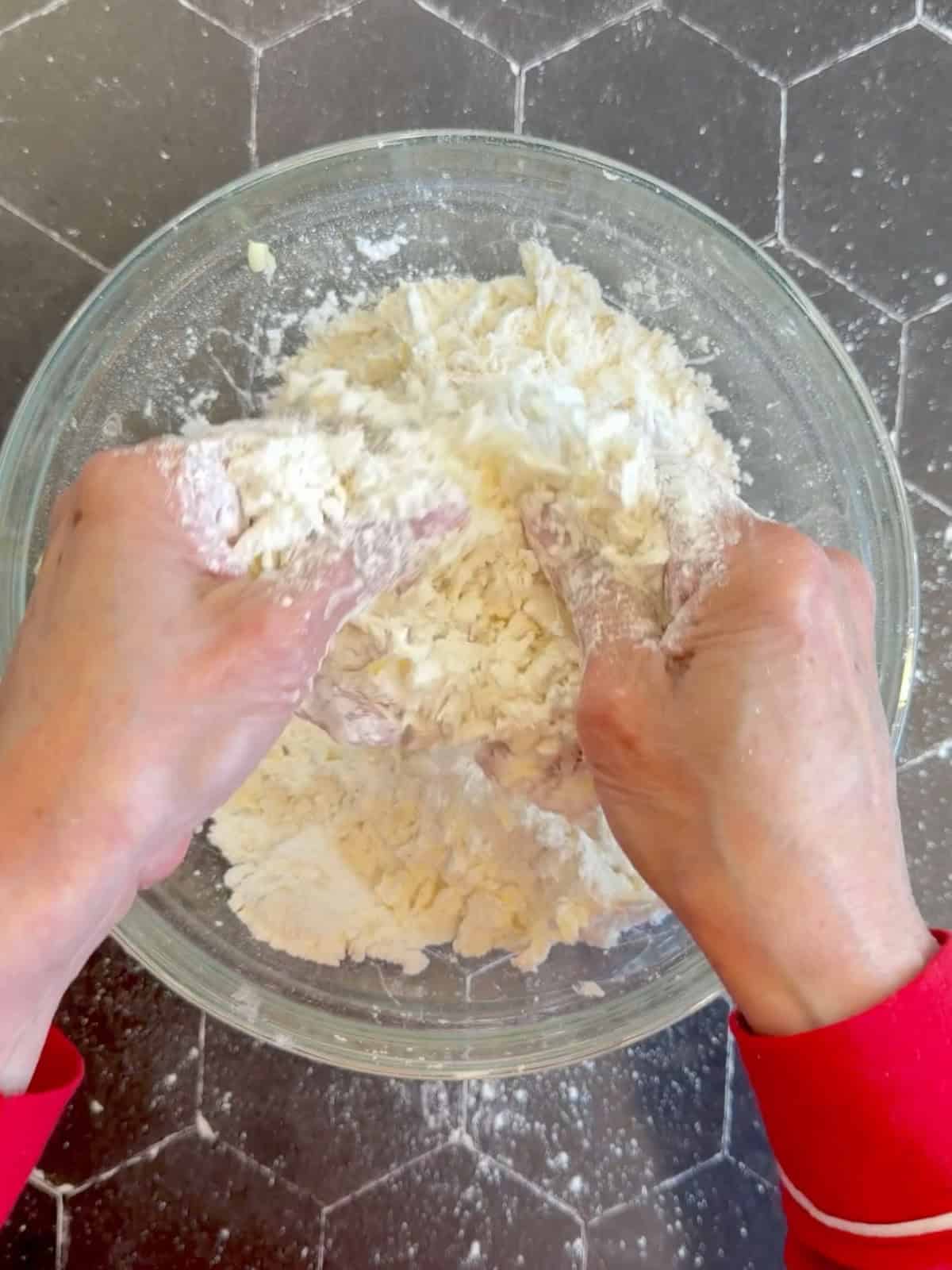Using a finger snapping motion to cut butter into dry ingredients in a glass bowl to make biscuits.