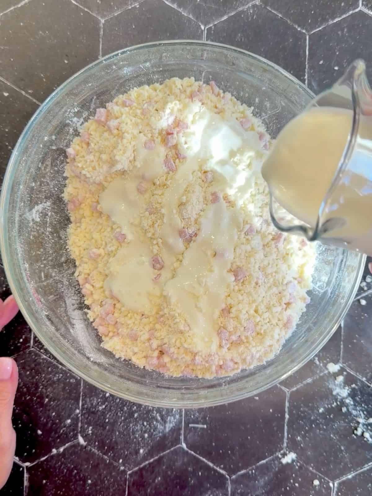 Pouring buttermilk into dry ingredients in a glass bowl.