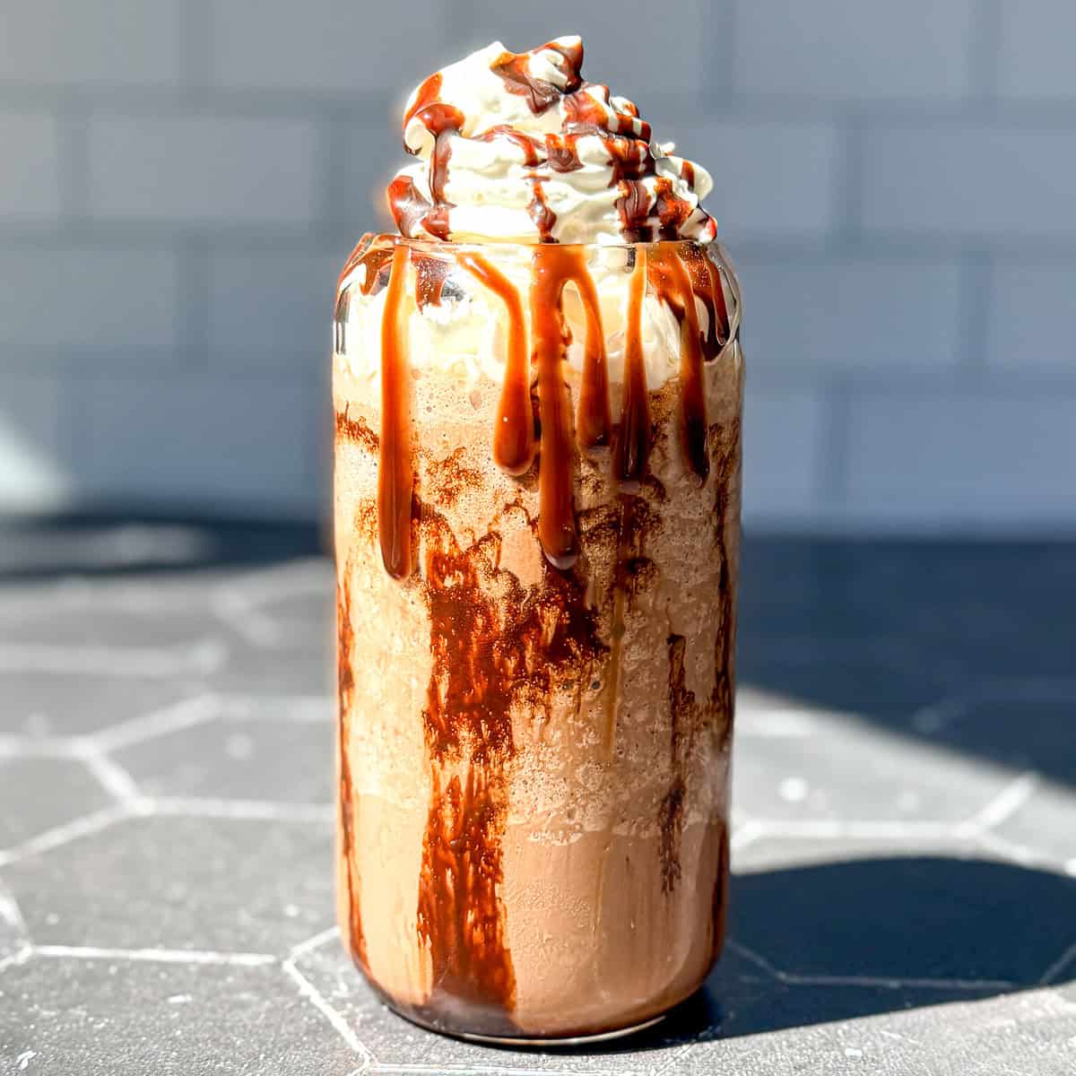 Mocha Frappuccino on a black counter with a subway tile backdrop.
