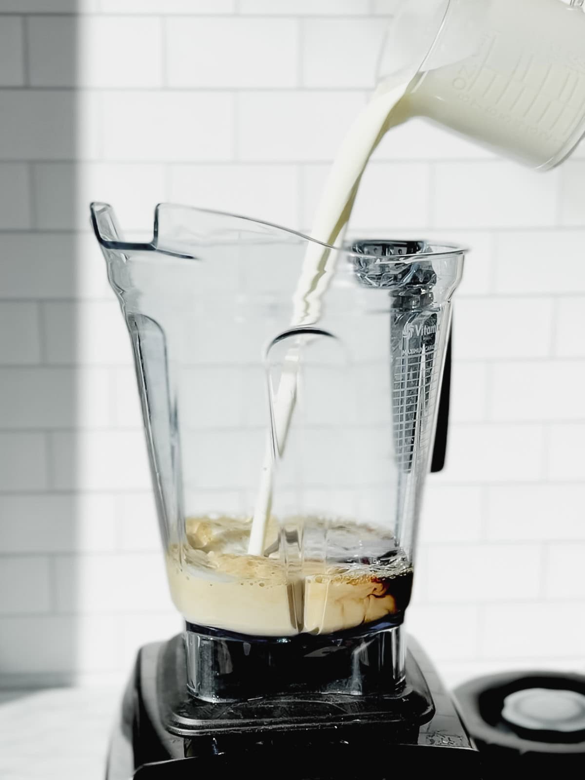Pouring milk into coffee in a blender.