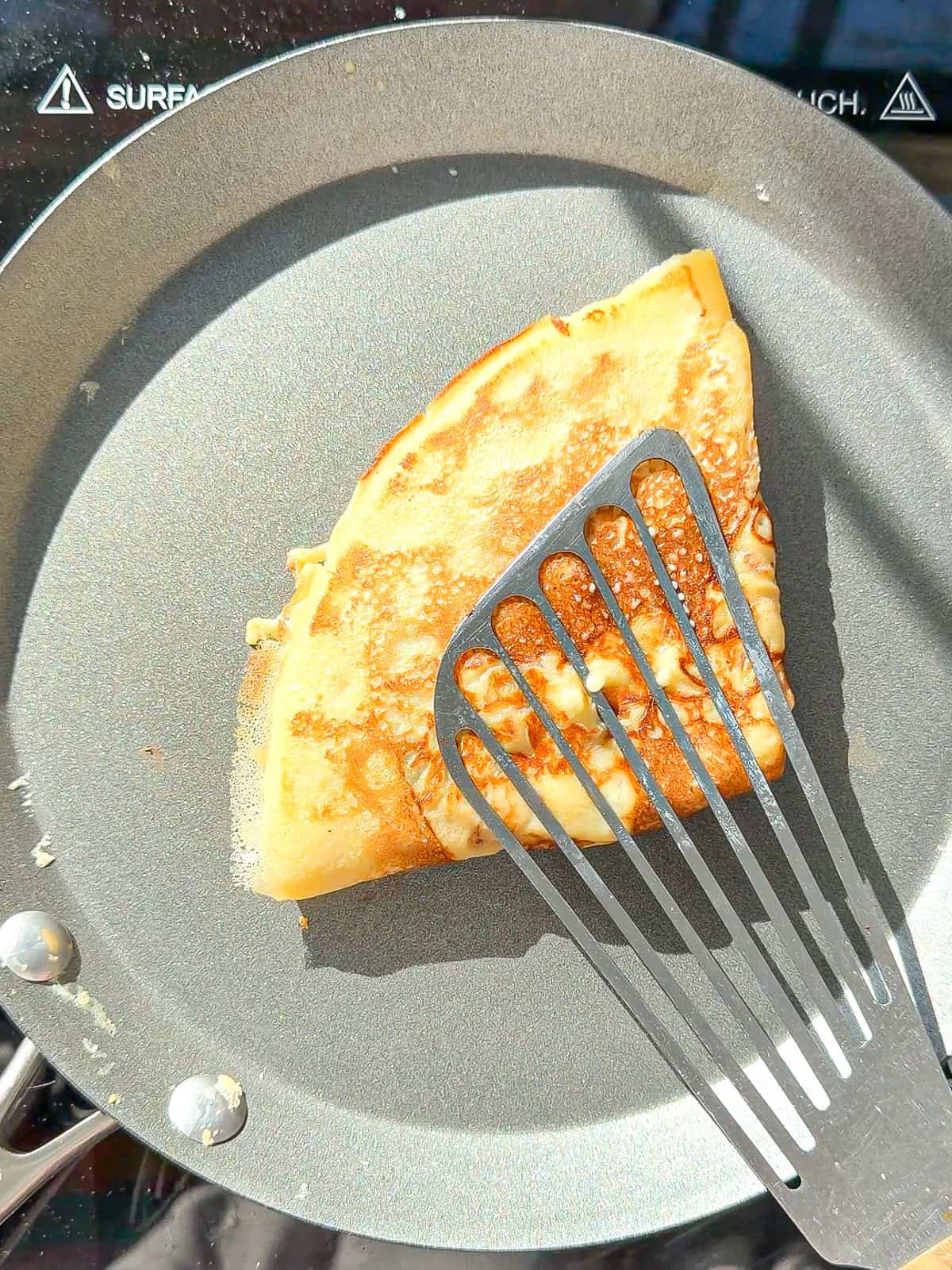 A triangular folded crêpe and a grey pan with a silver spatula.