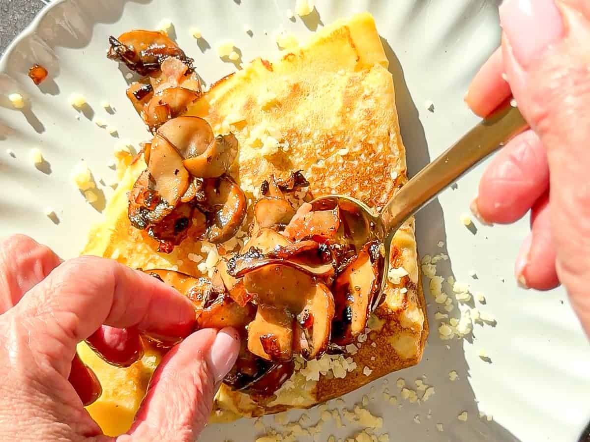 Spooning mushrooms on top of a triangular folded crêpe.