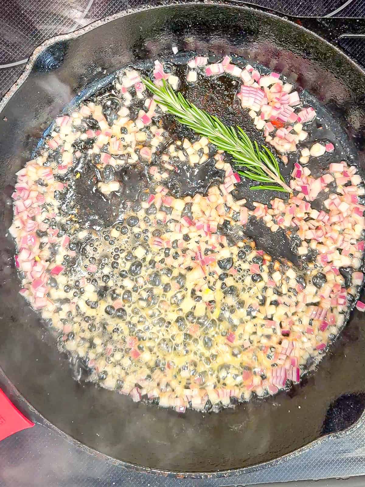 A sprig of rosemary and onion sautéed in a black pan.