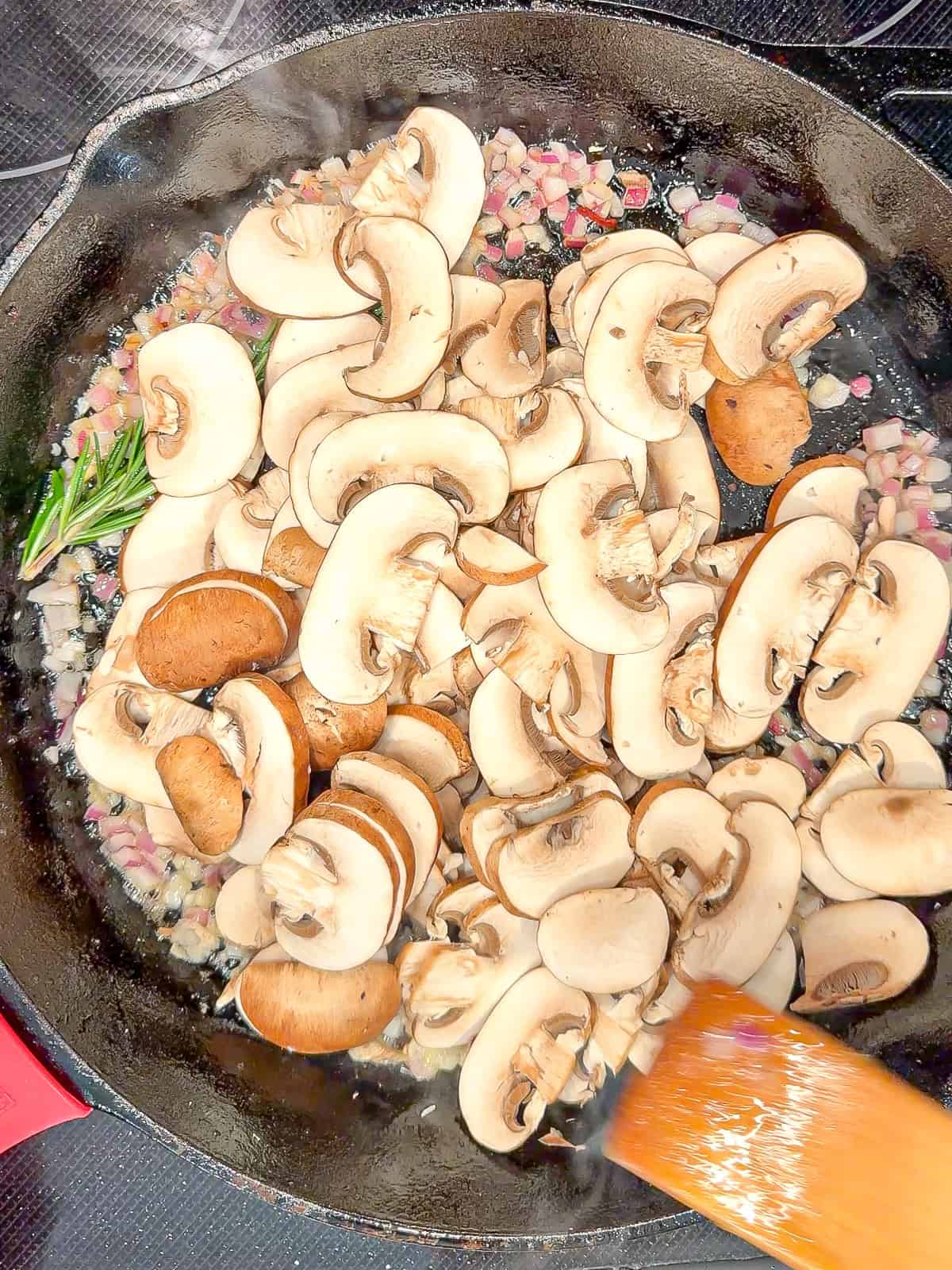 Mushrooms added to a black pan with rosemary and onion.