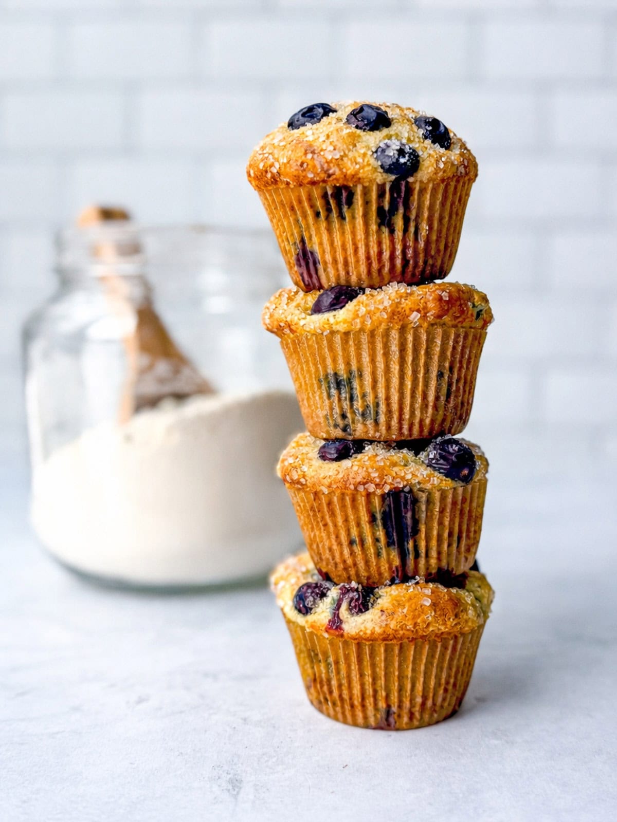 A snack of blueberry pancake muffins in front of a glass jar of pancake mix.
