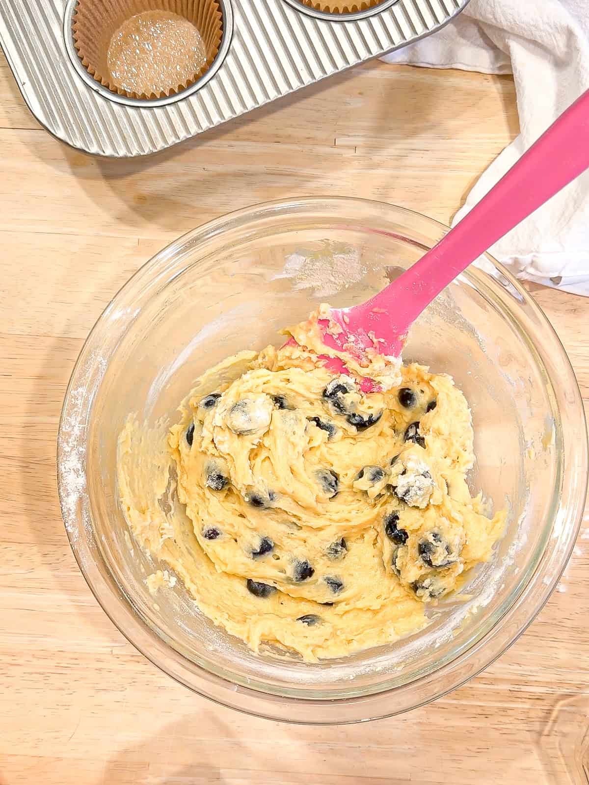 Blueberry muffin batter in a glass bowl with a pink spatula.