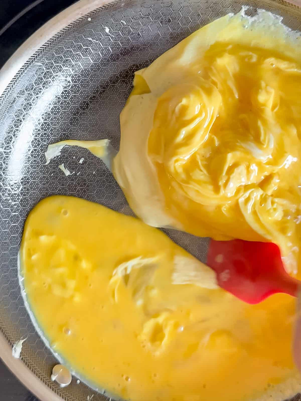 Making scrambled eggs in a black pan with a red spatula.