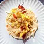 Bacon egg and potato breakfast taco on a tan plate.