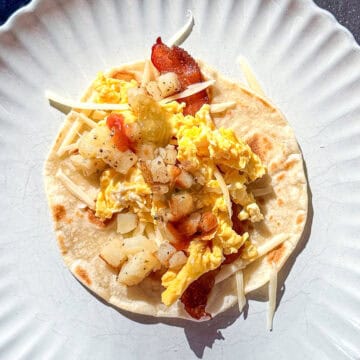 Bacon egg and potato breakfast taco on a tan plate.