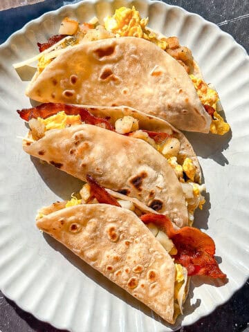 Three breakfast tacos on a tan plate.