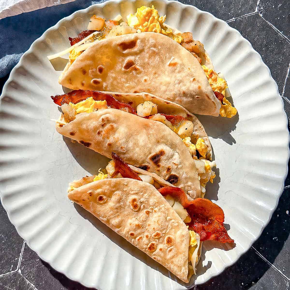 Three breakfast tacos on a tan plate.