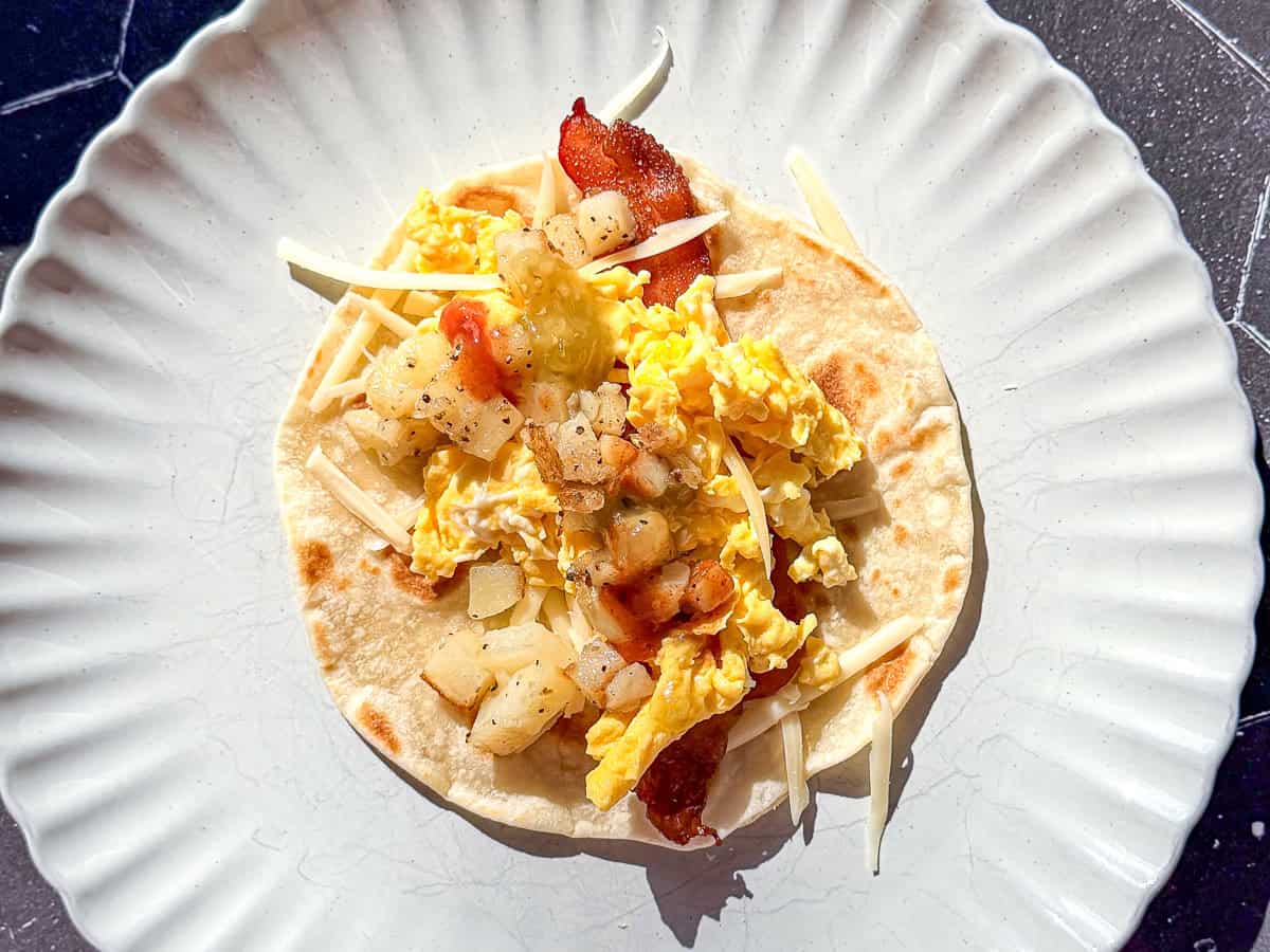 Bacon egg and potato breakfast taco on a tan plate.