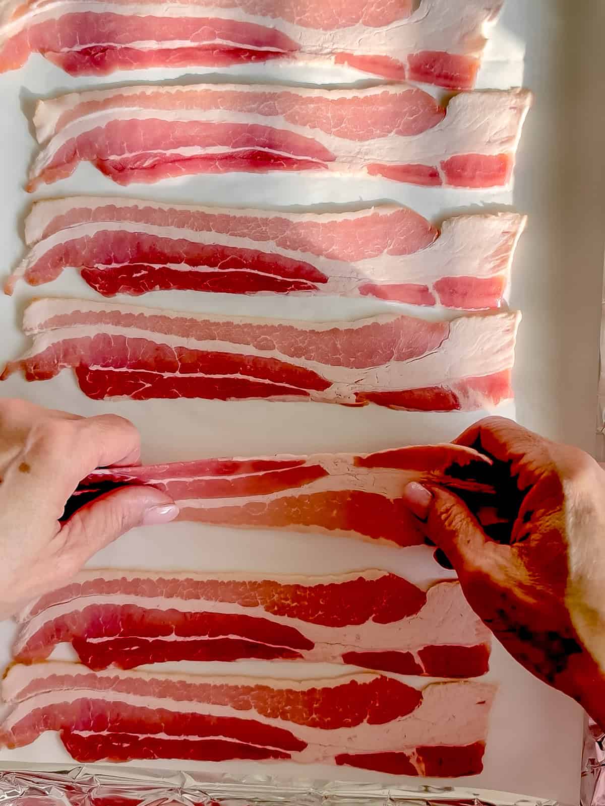 Laying raw strips of bacon on parchment paper.