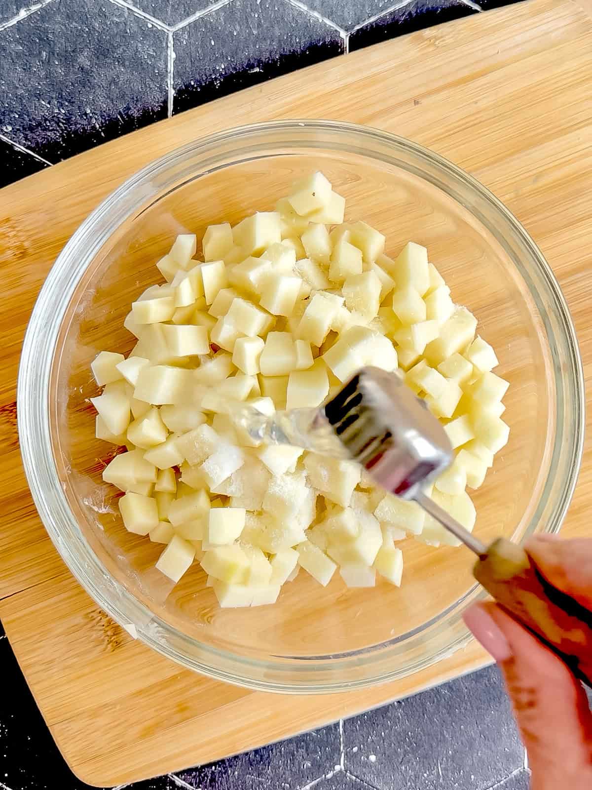 Adding water and salt to diced raw potatoes in a glass bowl.