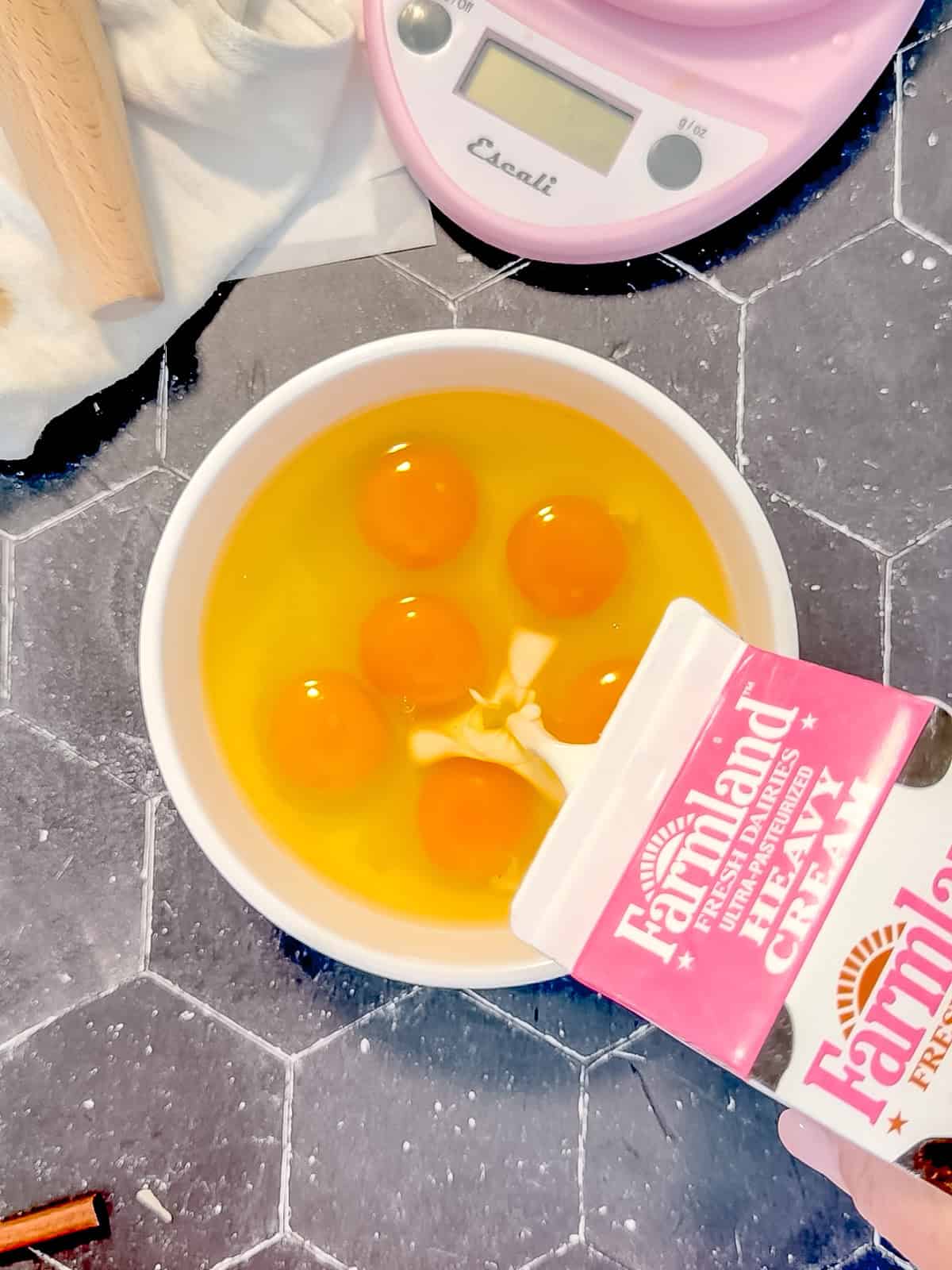 Pouring cream into a white bowl containing raw eggs.