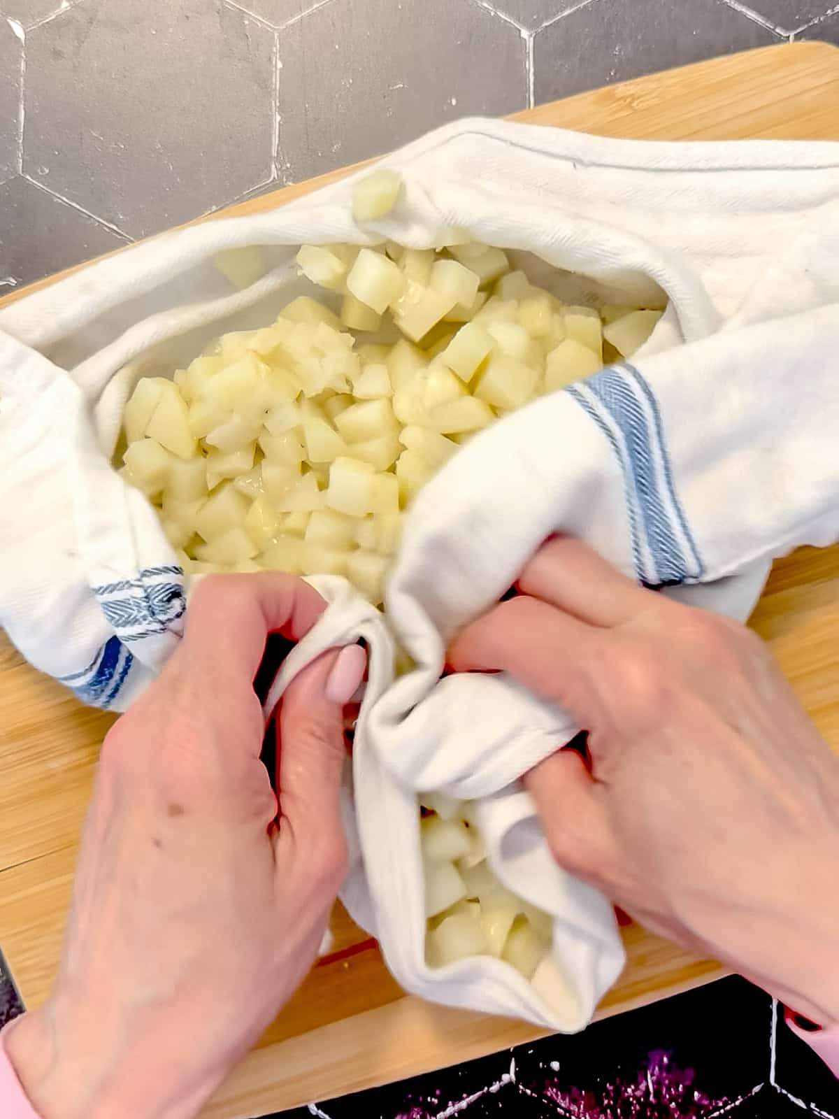 Drying off partially cooked diced potatoes in a kitchen towel.