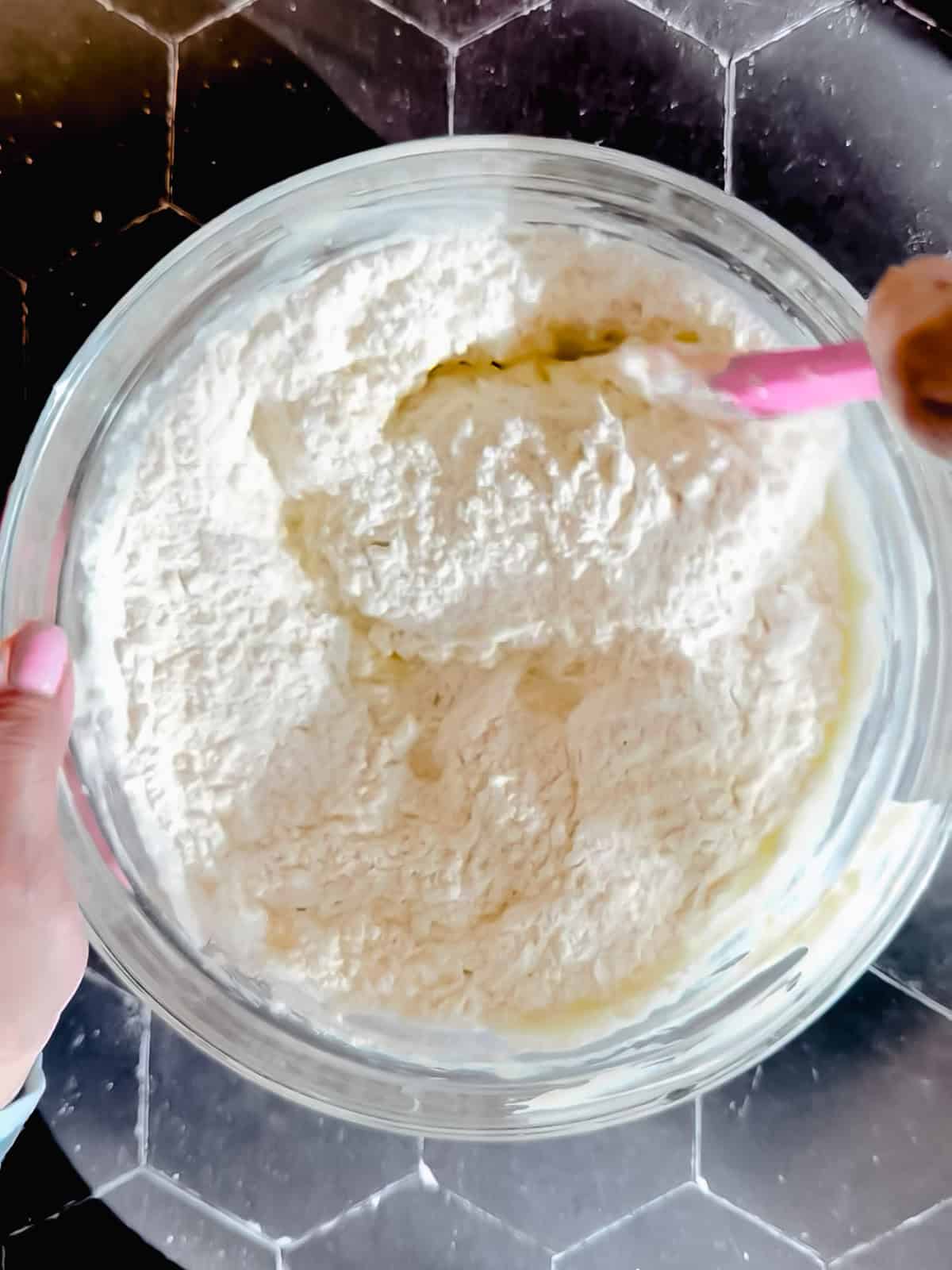 Using a pink spatula to mix pancake batter in a glass bowl.