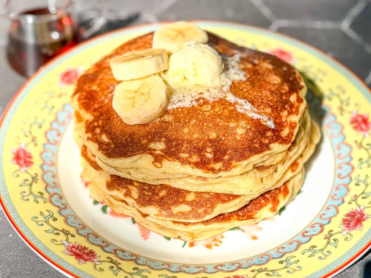A stack of banana oatmeal pancake pancakes on a yellow floral plate.