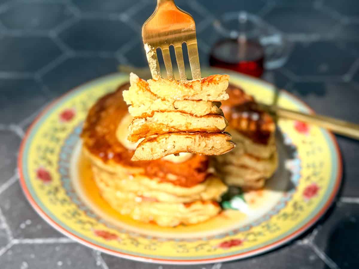 Side view of a fork holding a bite of banana oatmeal pancake with the remaining stack of pancakes in the background.