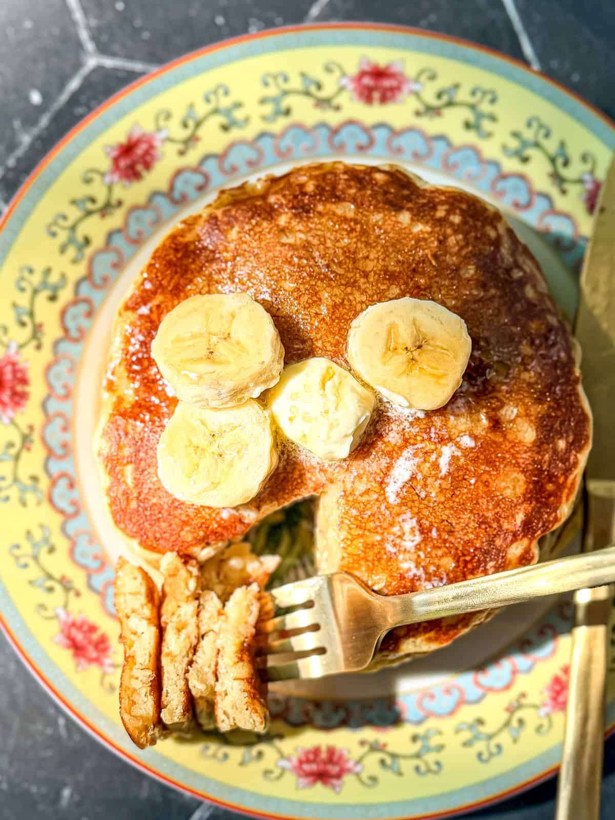 Top view of a stack of banana oatmeal pancake pancakes with bananas and a pat of butter on top.