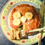 Top view of a stack of banana oatmeal pancake pancakes with bananas and a pat of butter on top.
