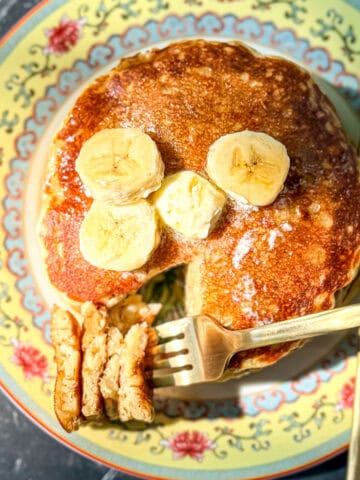 Top view of a stack of banana oatmeal pancake pancakes with bananas and a pat of butter on top.