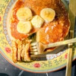 Top view of a stack of banana oatmeal pancake pancakes with bananas and a pat of butter on top.