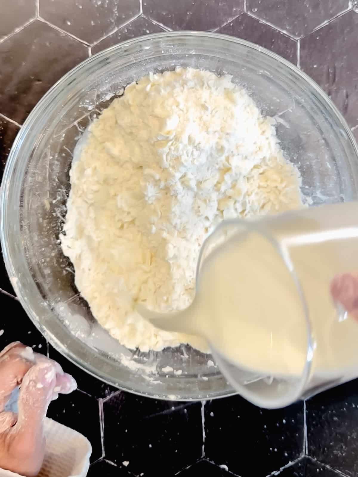 Adding milk to dry ingredients to make biscuits.