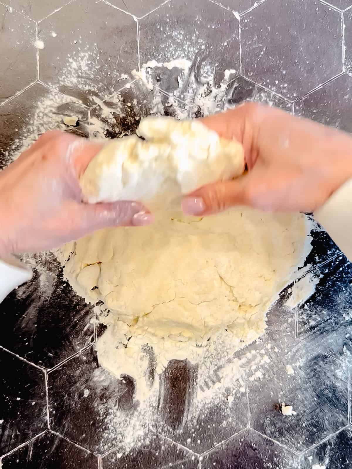 Folding biscuit dough over itself on a black surface.
