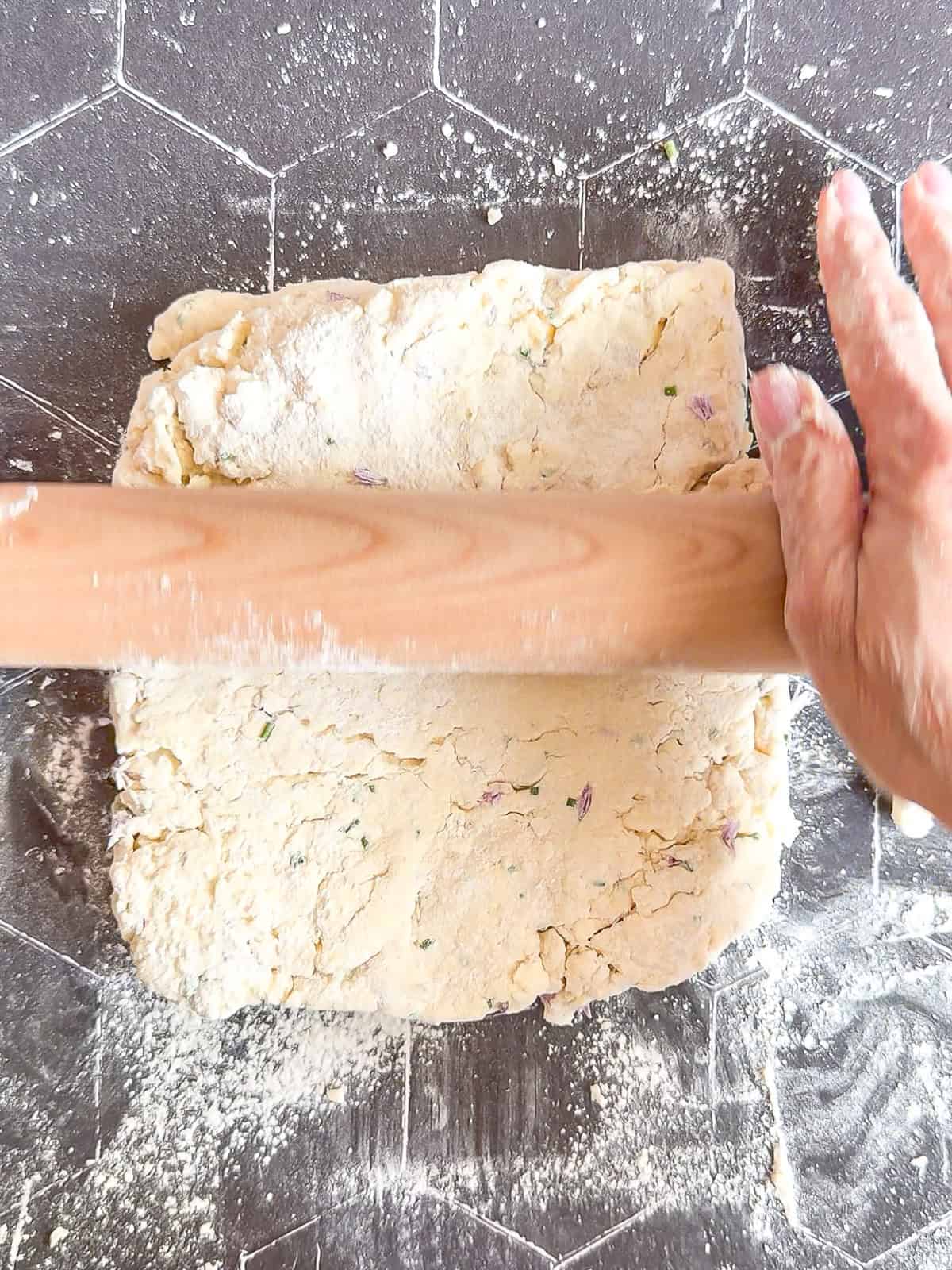 Rolling out biscuit dough on a black counter.