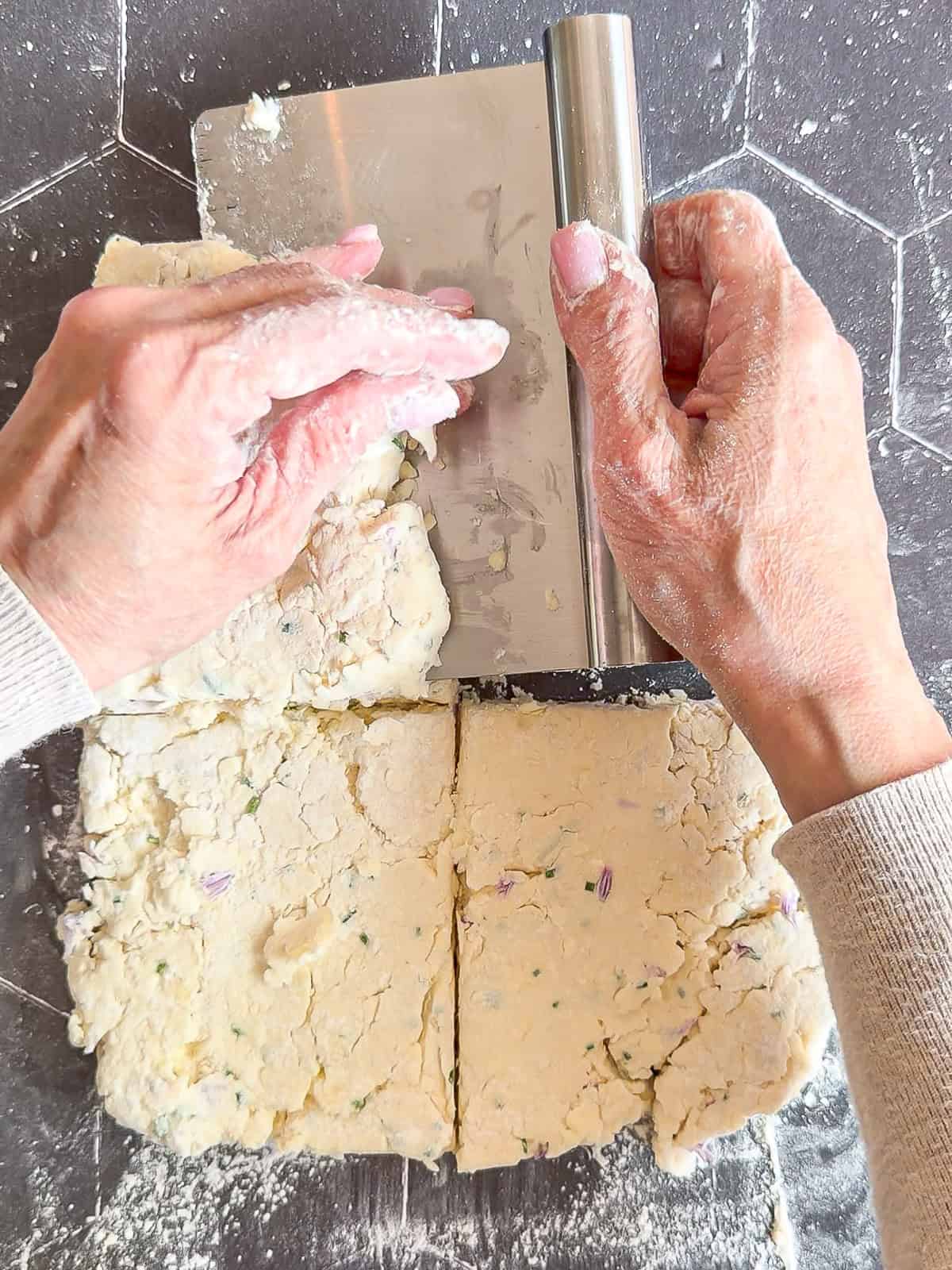 Using a bench scraper to stack squares of dough on top of each other.