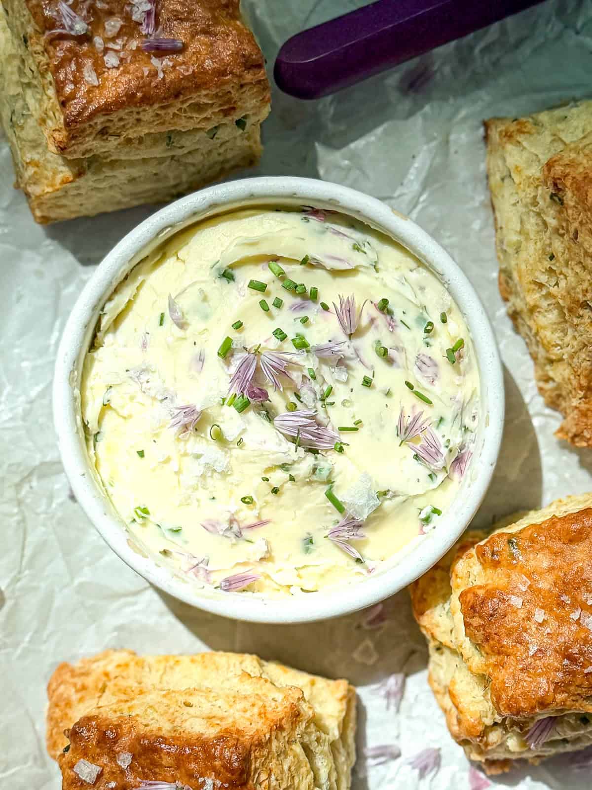 Chive blossom butter in a small ramekin with biscuits on parchment paper.