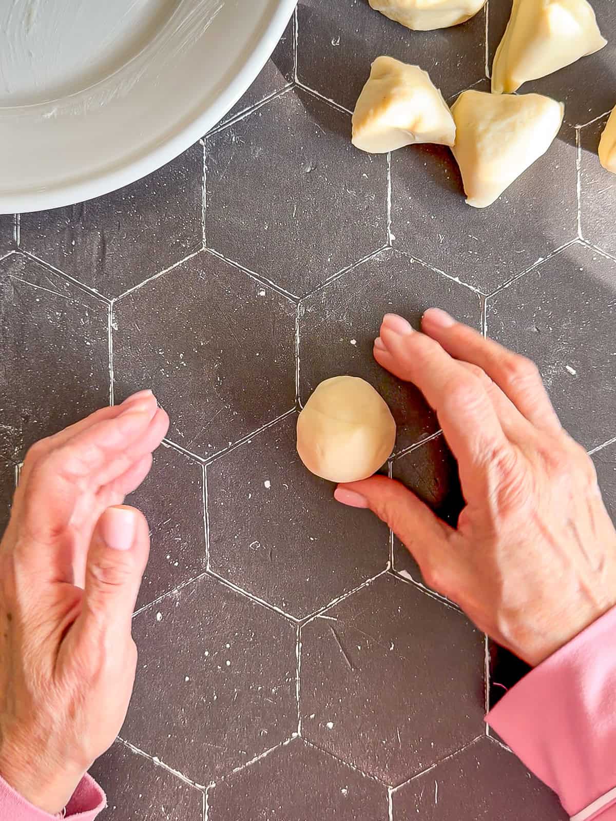 Rolling tortilla dough into a ball on a black tile counter.