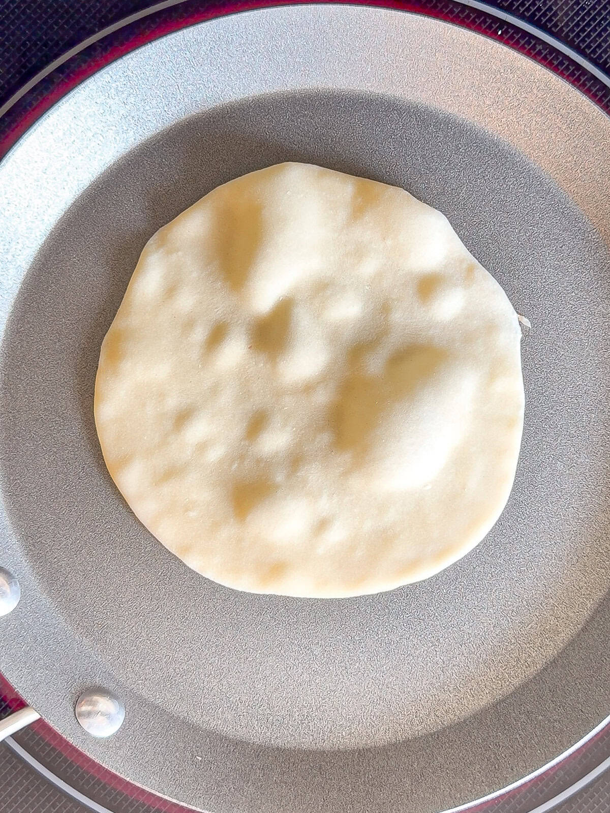 Cooking a flour tortilla in a silver pan.