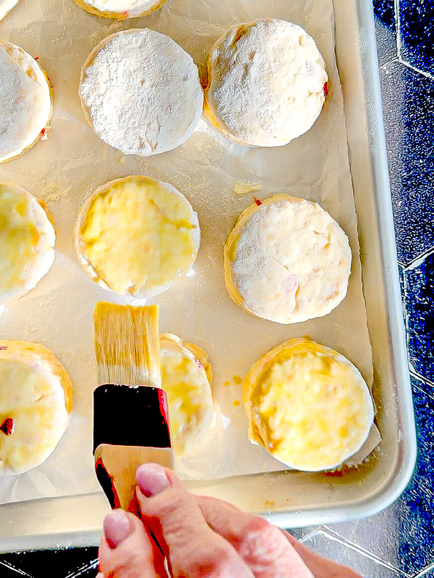 Brushing an egg wash on top of pimento cheese biscuits before baking.