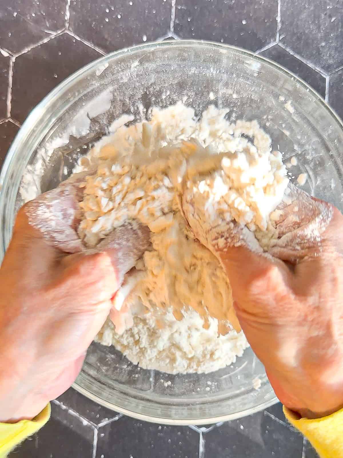 Cutting butter into flour mixture in a glass bowl on a black background.