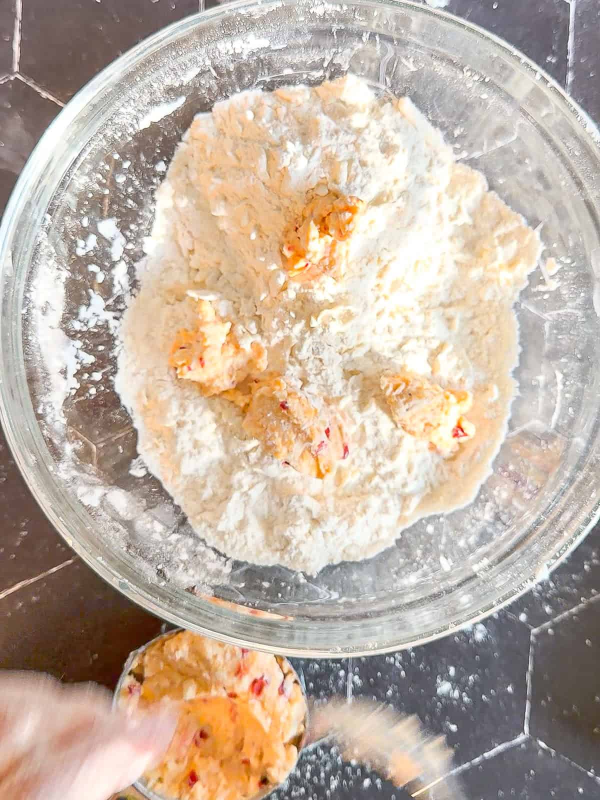 Adding teaspoons of pimento cheese to flour and butter mixture in a glass bowl.