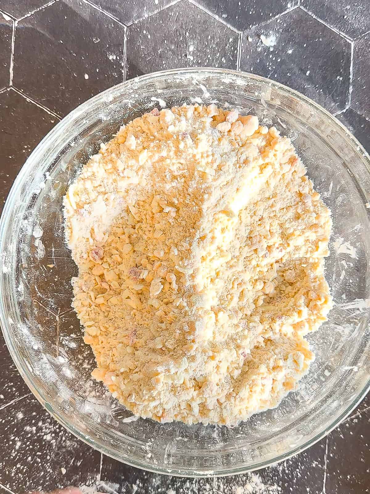 Flour mixture, butter, and pimento cheese mixed together in a glass bowl on a black counter.