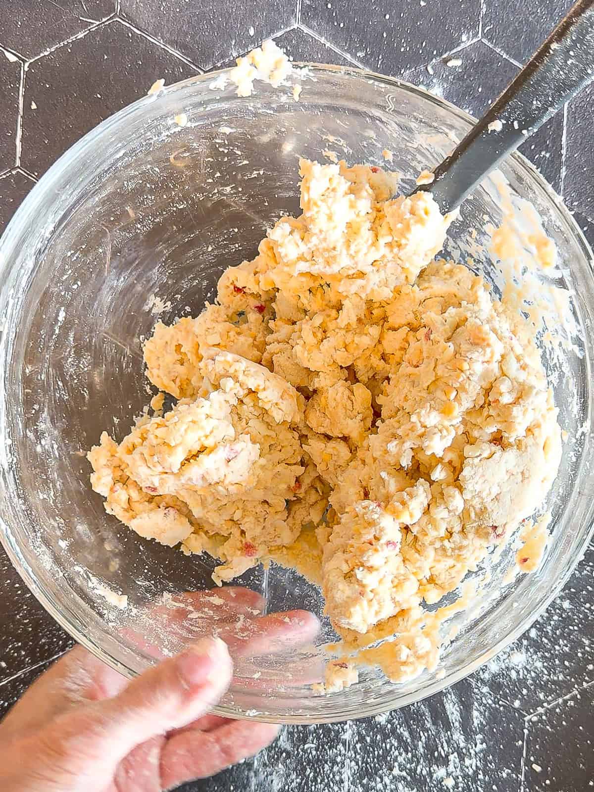 Pimento cheese biscuit dough in a glass bowl on a black background.