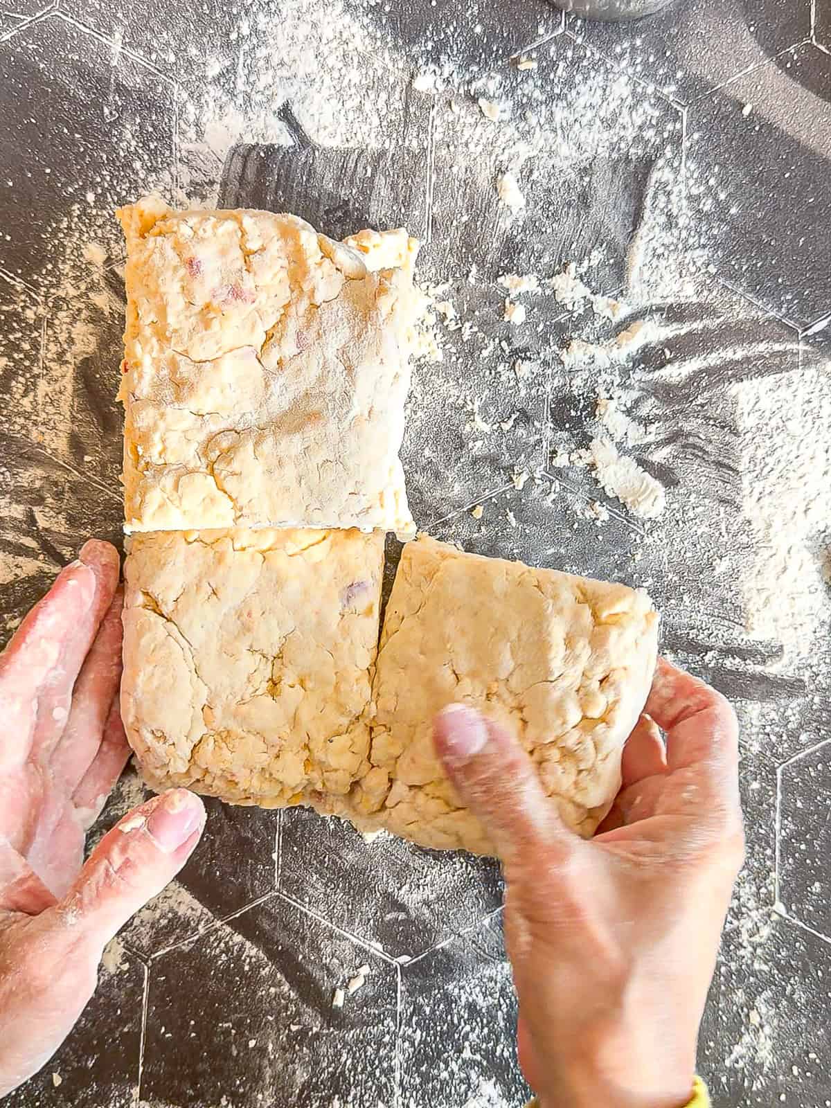 Stacking quarters of biscuit dough on top of each other on a black background.