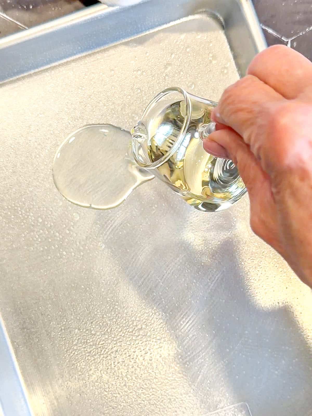 Pouring oil onto a sheet pan.
