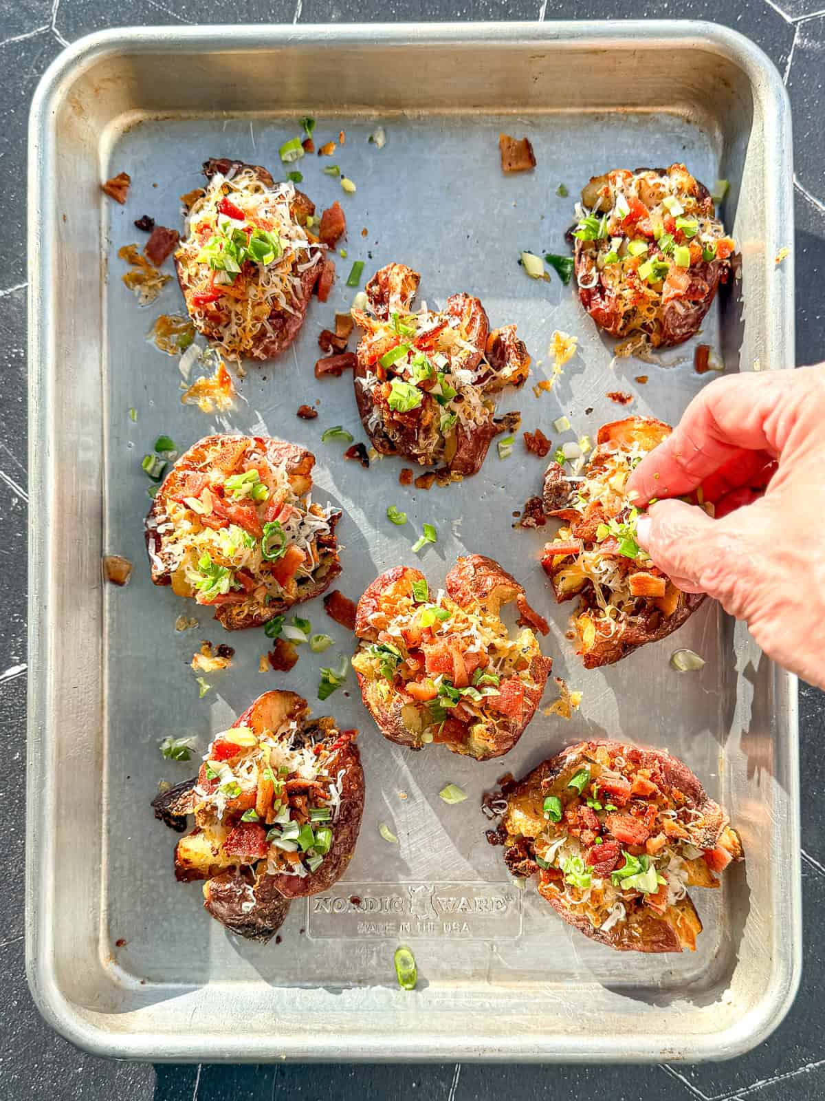 Sprinkling chives and bacon on top of crispy smashed breakfast potatoes.