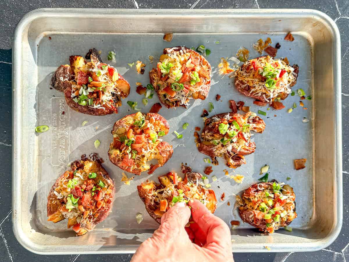 Sprinkling chives and bacon on top of crispy smashed breakfast potatoes.