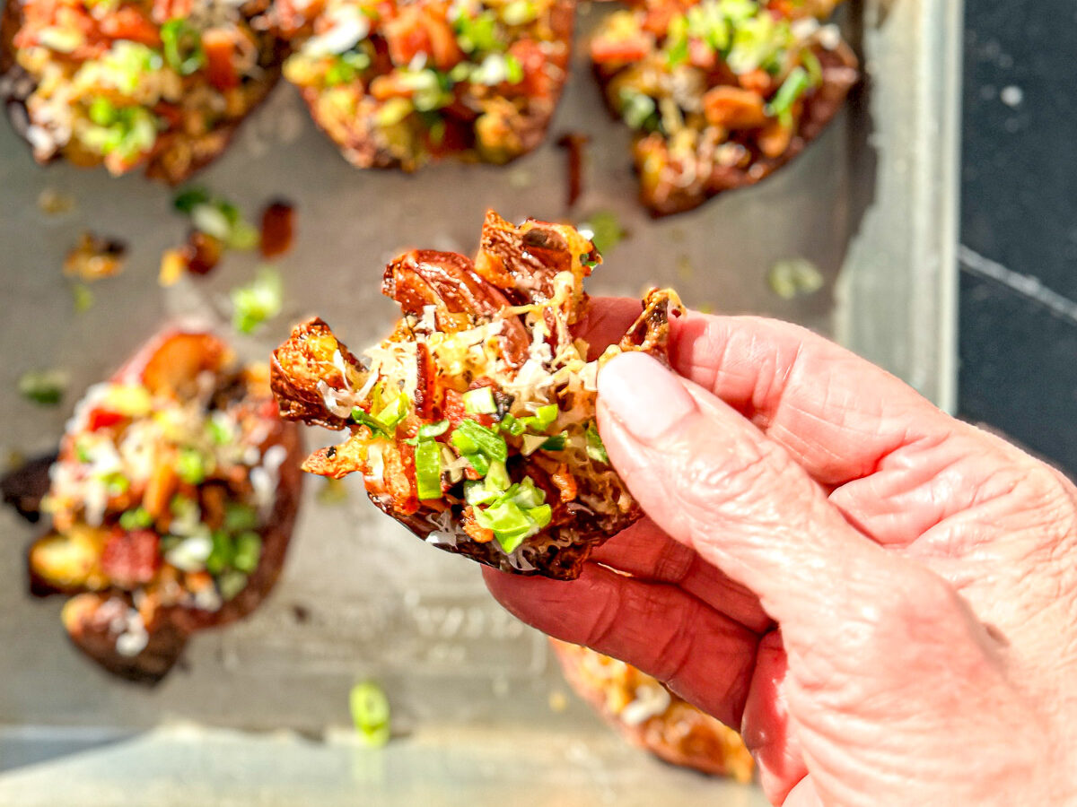 Hand holding a loaded crispy smashed potato.