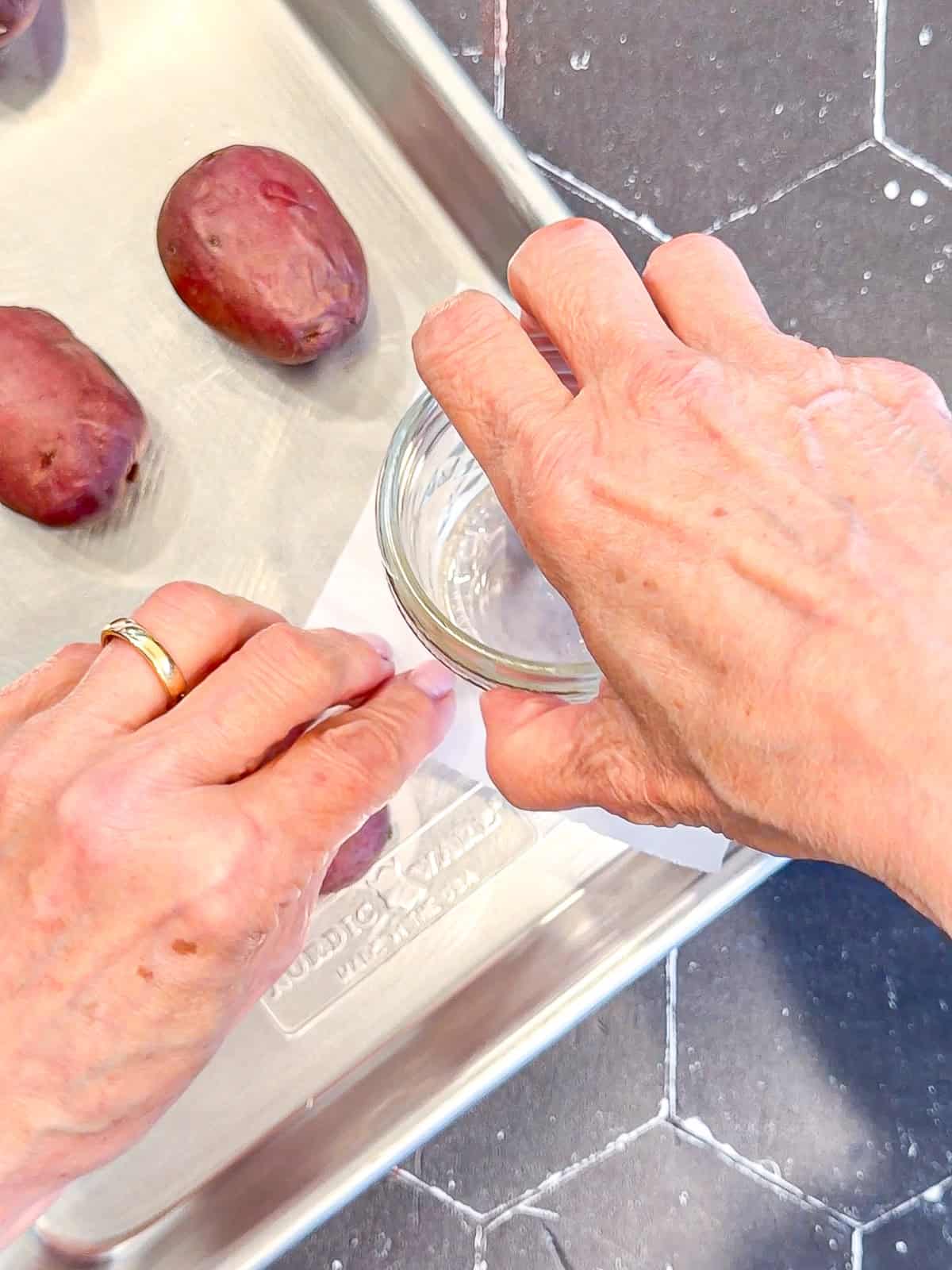 Using a mason jar and a piece of parchment paper to smash small red potatoes on a sheet pan.