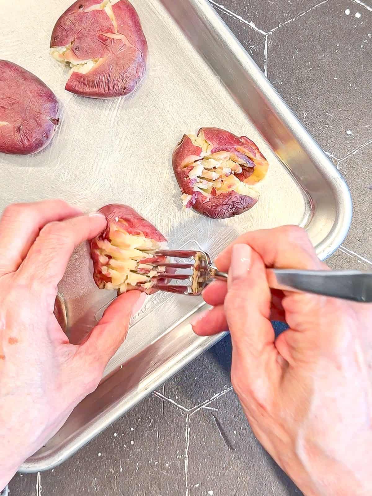 Using a fork to rough up the tops of potatoes on a sheet pan.